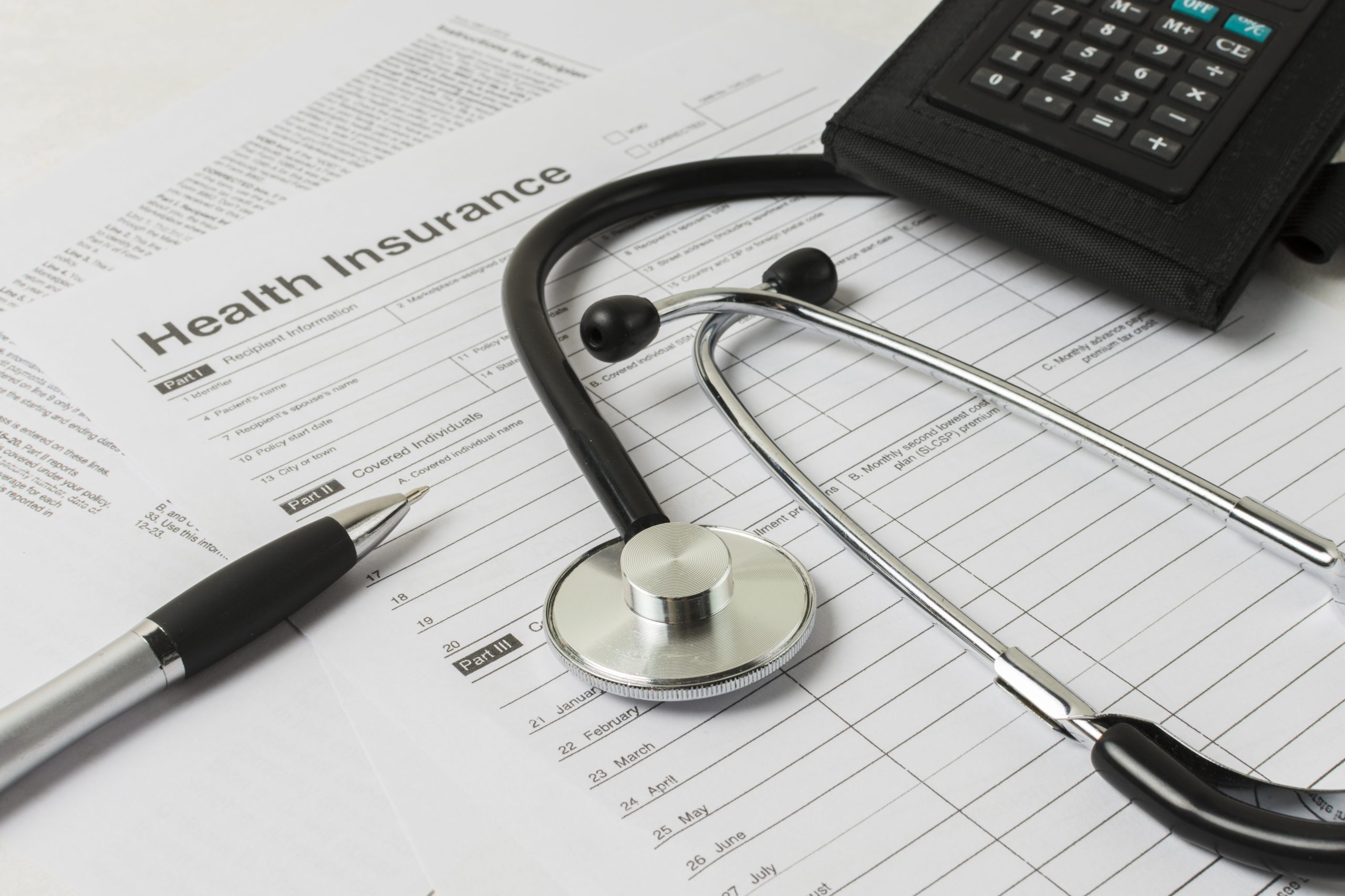 Stethoscope, calculator, and pen resting on insurance form.